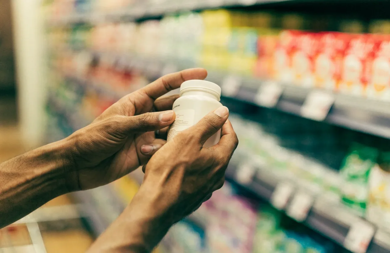 Manos de un comprador girando un frasco de suplemento para leer la información del reverso en la tienda